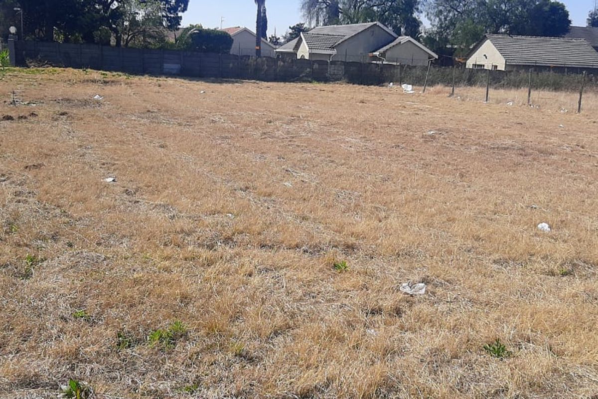 A vacant residential plot featuring dry grass, perimeter walling, and wire fencing, offering a clear space for future development.