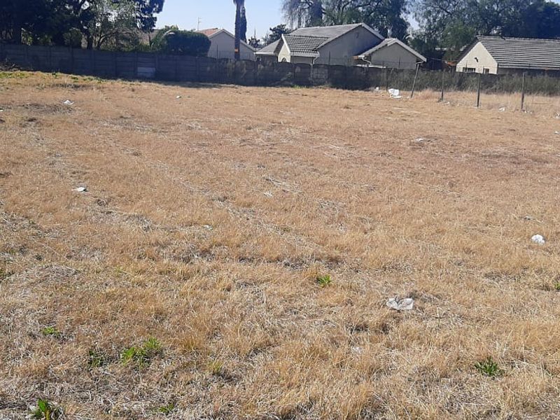 A vacant residential plot featuring dry grass, perimeter walling, and wire fencing, offering a clear space for future development.