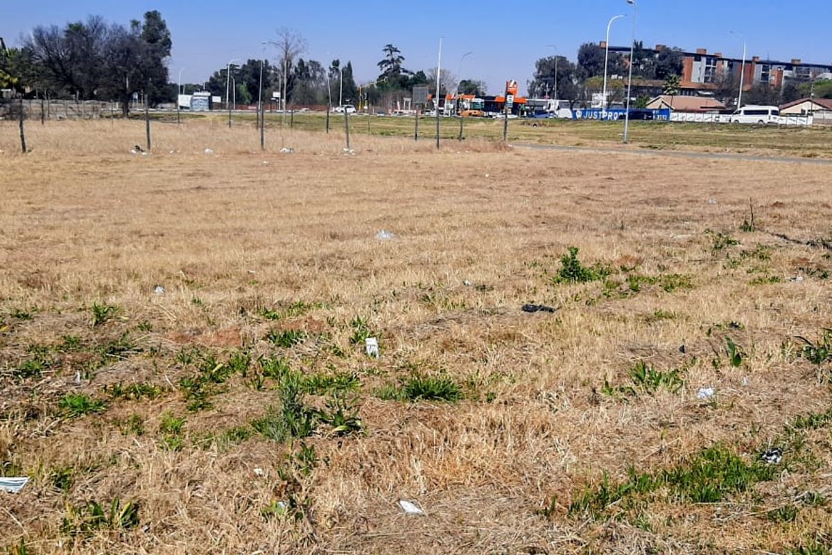 A vacant residential plot of land featuring dry grass, perimeter wire fencing, and a utility pole, situated in an open suburban area.