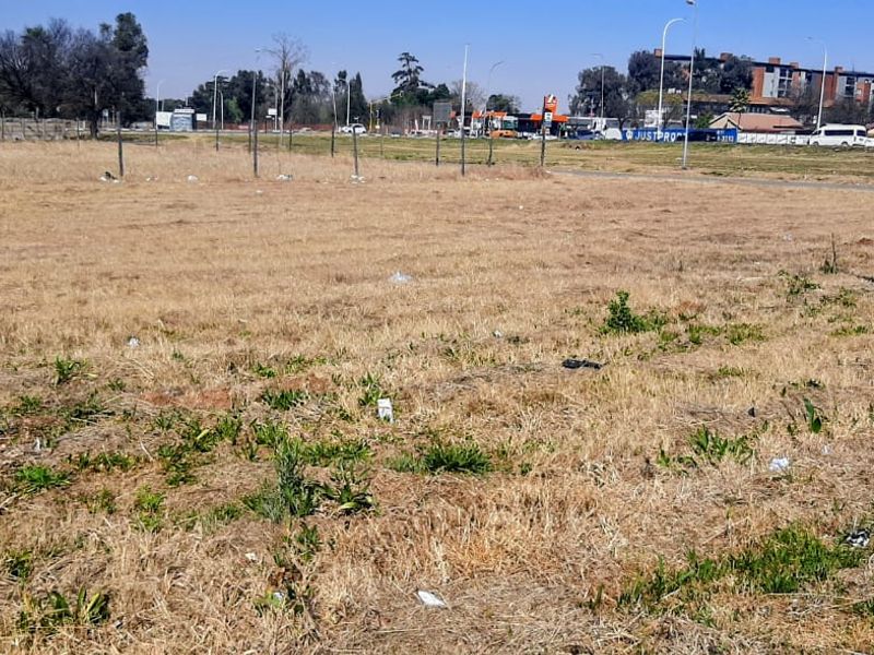 A vacant residential plot of land featuring dry grass, perimeter wire fencing, and a utility pole, situated in an open suburban area.