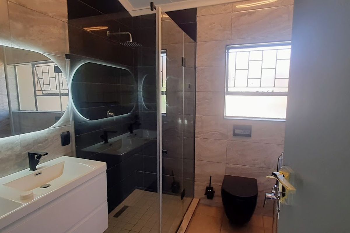 Modern bathroom featuring a double vanity, walk-in shower with glass enclosure, wall-mounted toilet, and stylish backlit mirror with contemporary tiled finishes.