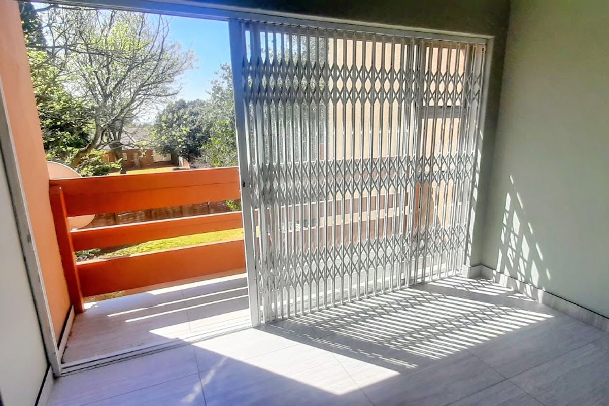 An empty bedroom featuring tiled flooring and a sliding glass door with a security gate leading out to a private balcony.