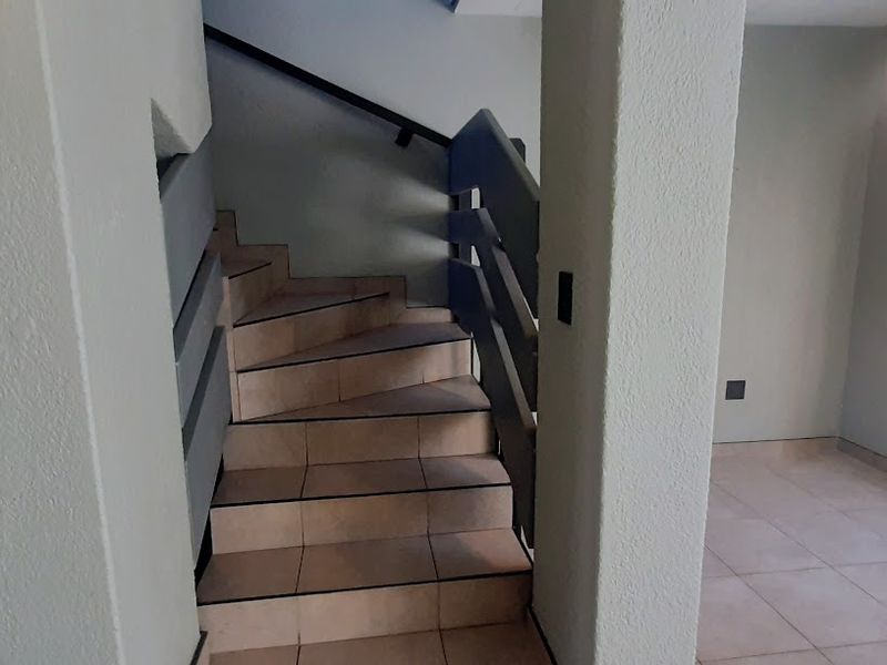 A bright hallway featuring a tiled staircase with a metal handrail and a secure entrance door with a metal security gate.