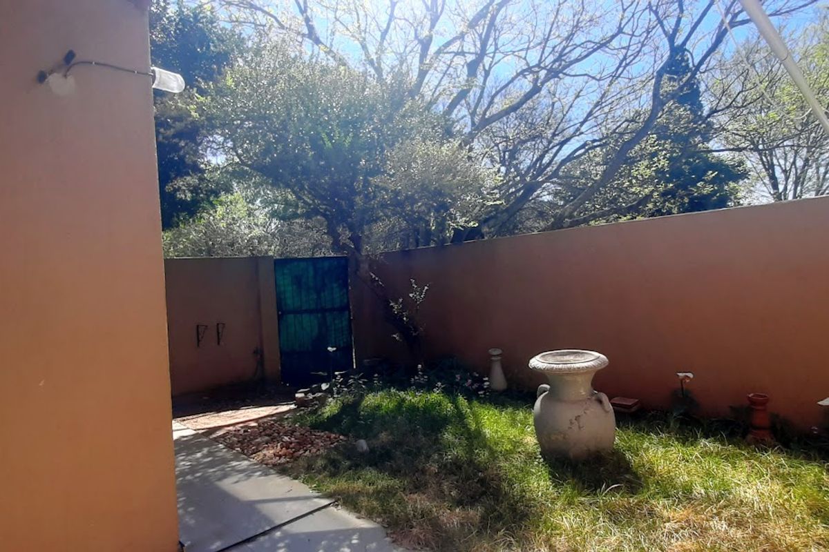 A private rear courtyard featuring a paved walkway, boundary walls, and a metal access gate, offering potential for landscaping and outdoor living improvements.