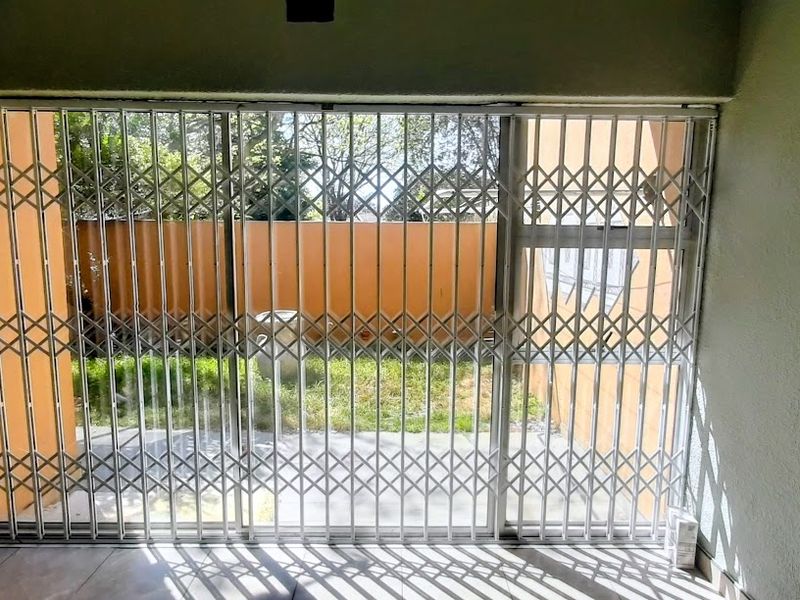 A covered patio area featuring tiled flooring and a secure sliding gate, providing direct access to the rear garden space.