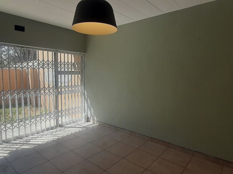 An empty living room featuring tiled flooring, a pendant light, and a sliding glass door with a security gate leading to the exterior.
