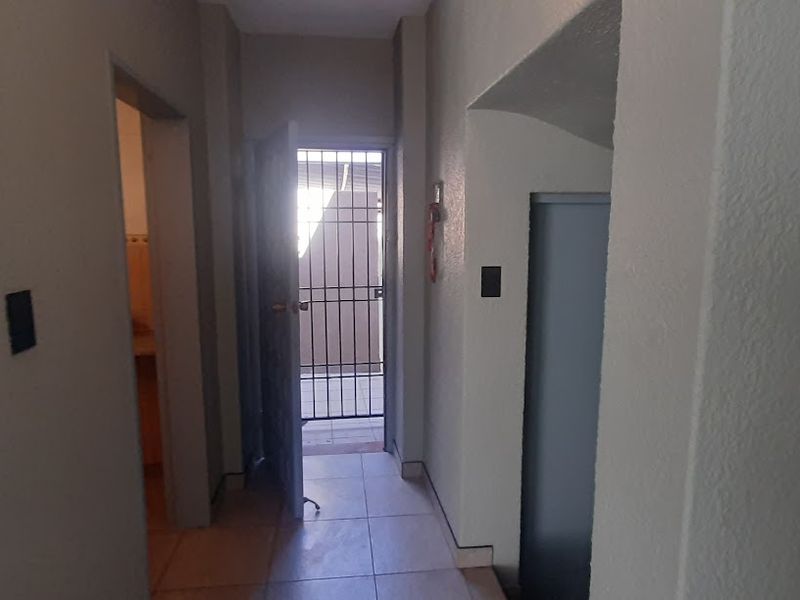 A functional hallway with tiled flooring, providing access to adjacent rooms and an exterior security gate.