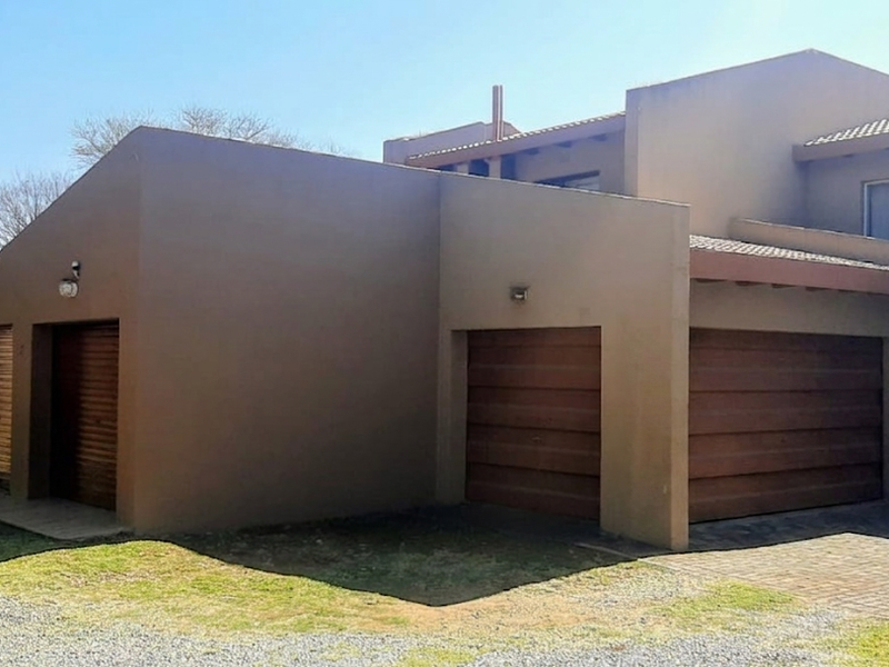 Exterior view of a townhouse featuring a combination of single and double garages with paved driveway access and neutral rendered facade.