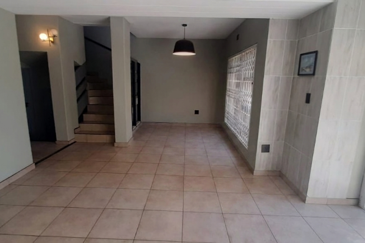 An open-plan living area featuring neutral tiled flooring, a staircase, and a tiled feature wall, providing a clean and versatile space.
