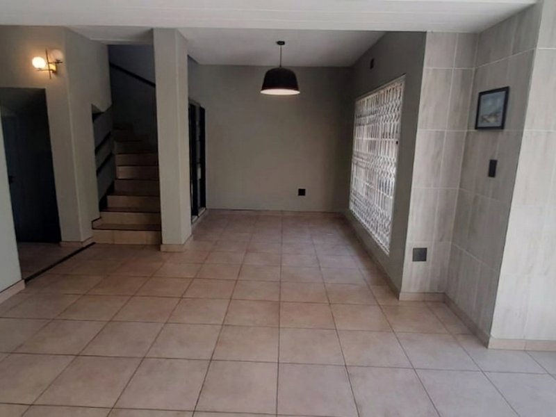 An open-plan living area featuring neutral tiled flooring, a staircase, and a tiled feature wall, providing a clean and versatile space.