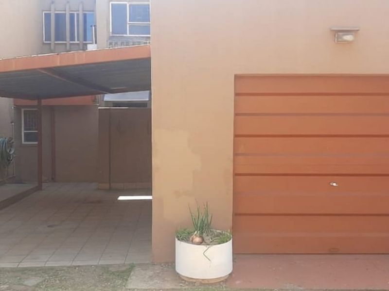 Front exterior view of the townhouse featuring a single garage and an attached carport with paved driveway area.