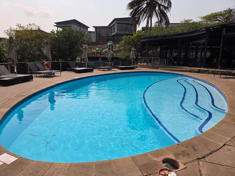 A well-maintained swimming pool area featuring timber decking, a paved surround, and an adjacent covered patio space.