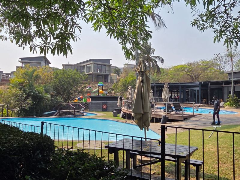 A communal outdoor pool area featuring a swimming pool, wooden decking, and a children's play area set within a landscaped estate environment.