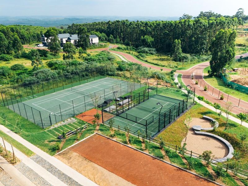 Aerial view of a well-maintained sports facility featuring a tennis court and a padel court set within a landscaped residential estate.