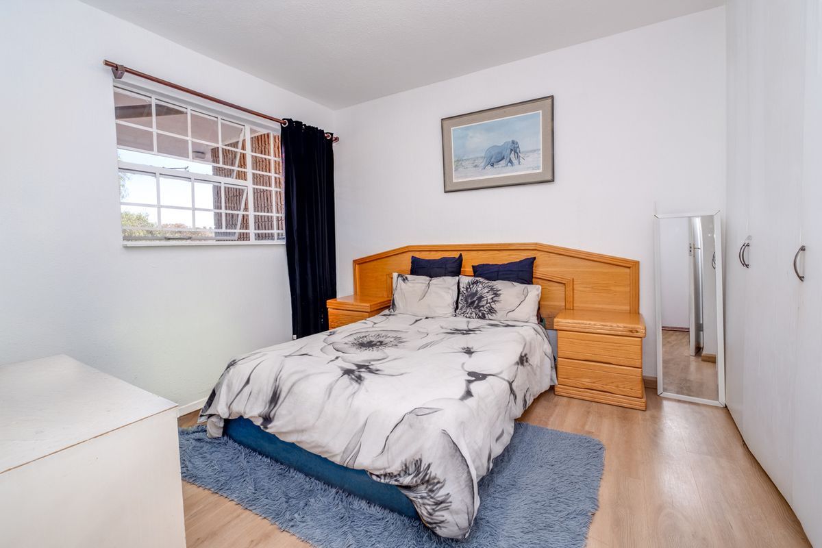 A well-lit bedroom featuring laminate flooring, built-in cupboards, and a window fitted with security burglar bars.
