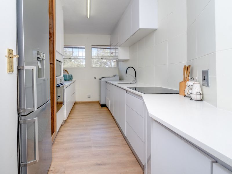 Modern galley-style kitchen featuring white cabinetry, quartz countertops, integrated electric hob, built-in oven, and a sleek undermount sink with a contemporary mixer tap.