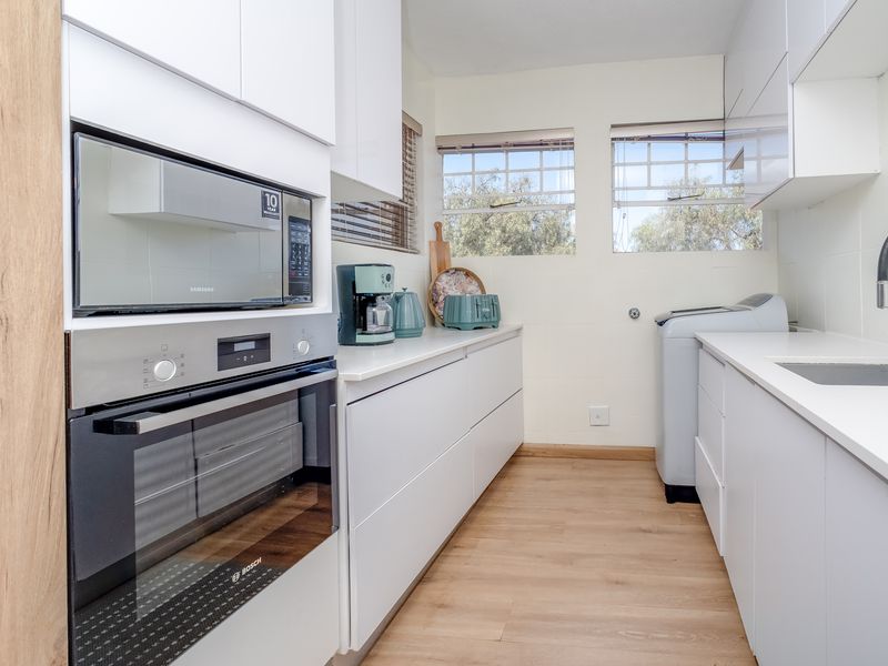 Modern, well-maintained scullery featuring sleek white cabinetry, stone countertops, integrated oven and microwave, and a functional sink area with contemporary fixtures.