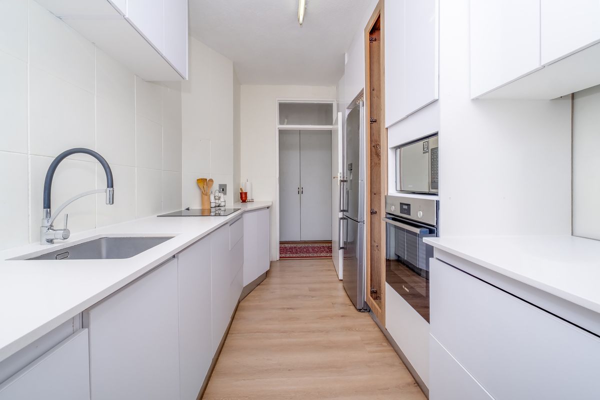 A modern, galley-style kitchen featuring white cabinetry, integrated appliances including an oven and microwave, and a sleek stainless steel sink with a contemporary tap.