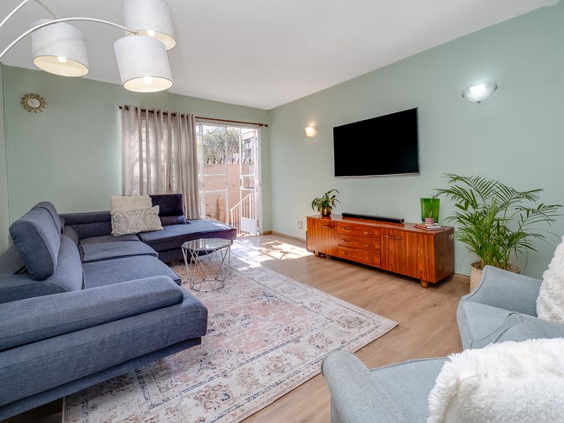 A bright and well-maintained living room featuring laminate flooring, soft green walls, and a sliding glass door providing access to the exterior.