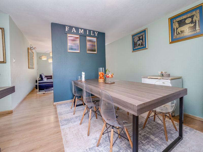 A well-lit dining area featuring laminate flooring and a bold blue accent wall, creating a distinct space within the open-plan layout.