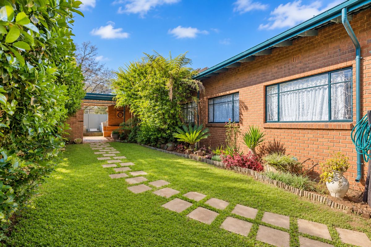 A well-maintained rear garden featuring a brick facade, established landscaping, and a stone pathway leading to a covered outdoor area.