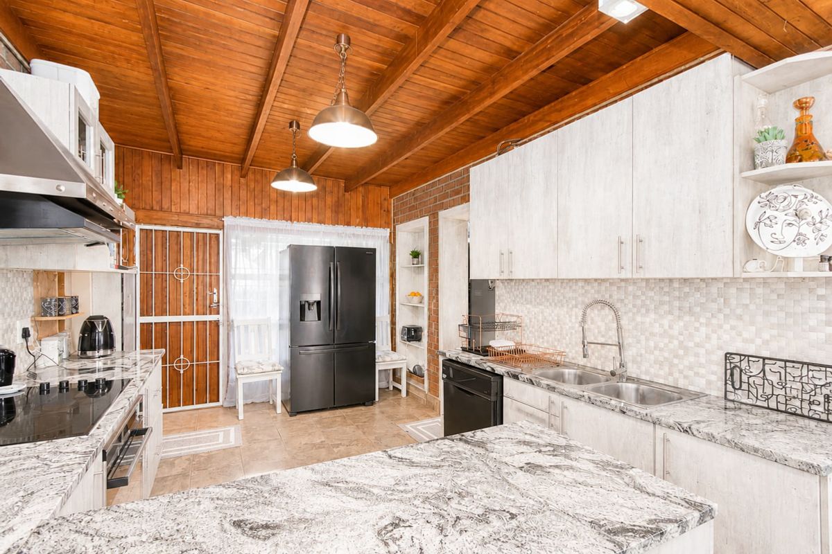 A well-appointed kitchen featuring granite countertops, exposed timber ceilings, brick accents, and modern cabinetry with integrated appliances.