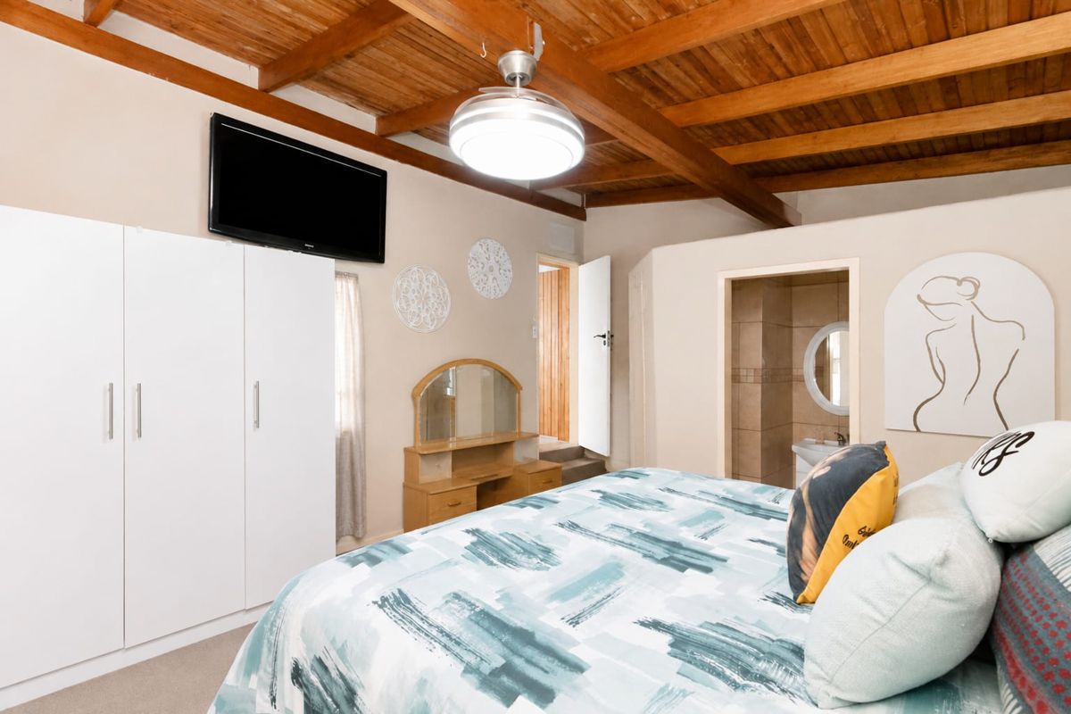 Spacious bedroom featuring exposed timber ceiling beams, built-in wardrobe storage, and direct access to an en-suite bathroom.