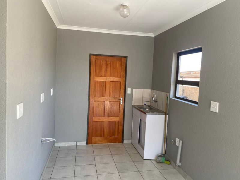 A clean, empty laundry room featuring tiled flooring, a built-in stainless steel sink with cabinet, and a timber door.