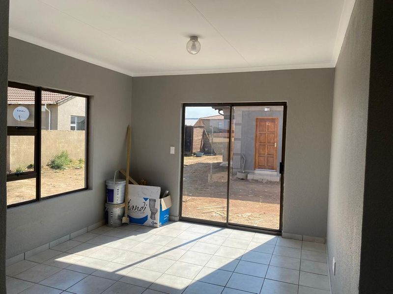 A bright, empty living area featuring neutral grey walls, tiled flooring, and large sliding glass doors providing access to the rear yard.