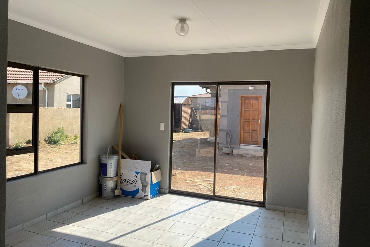 A bright, empty living area featuring neutral grey walls, tiled flooring, and large sliding glass doors providing access to the rear yard.