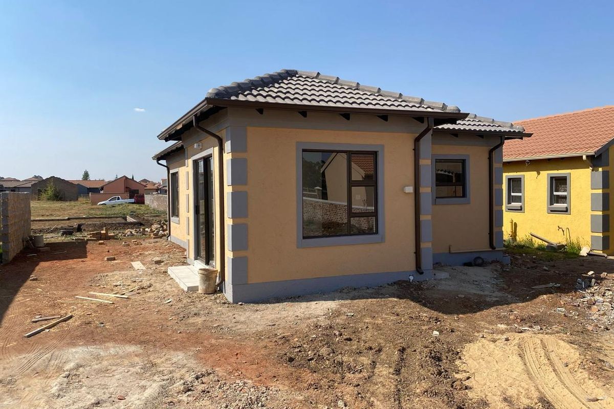 A view of the rear exterior of a newly constructed house featuring a tiled roof, aluminium window frames, and a sliding door.