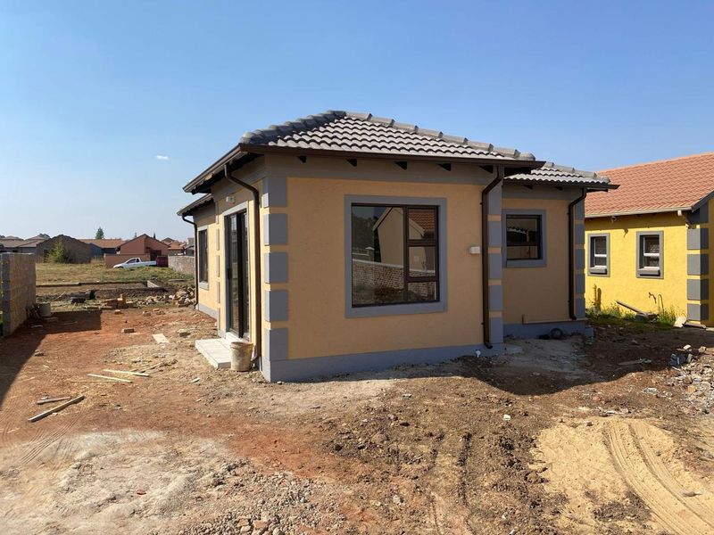 A view of the rear exterior of a newly constructed house featuring a tiled roof, aluminium window frames, and a sliding door.