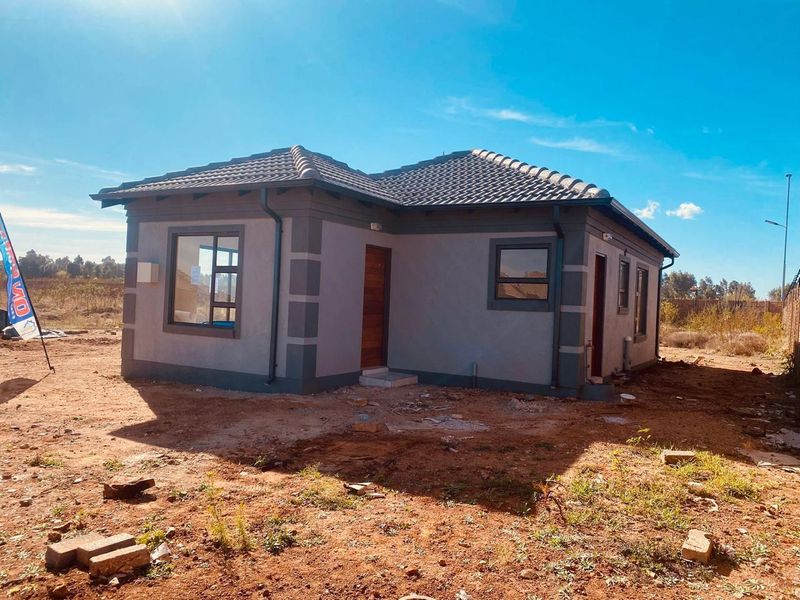 A newly constructed single-story house featuring a tiled roof, grey exterior finish with contrasting corner detailing, and aluminium window frames.