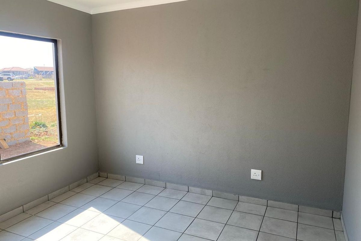 A clean, empty bedroom featuring neutral grey walls, tiled flooring, and a large window providing natural light.