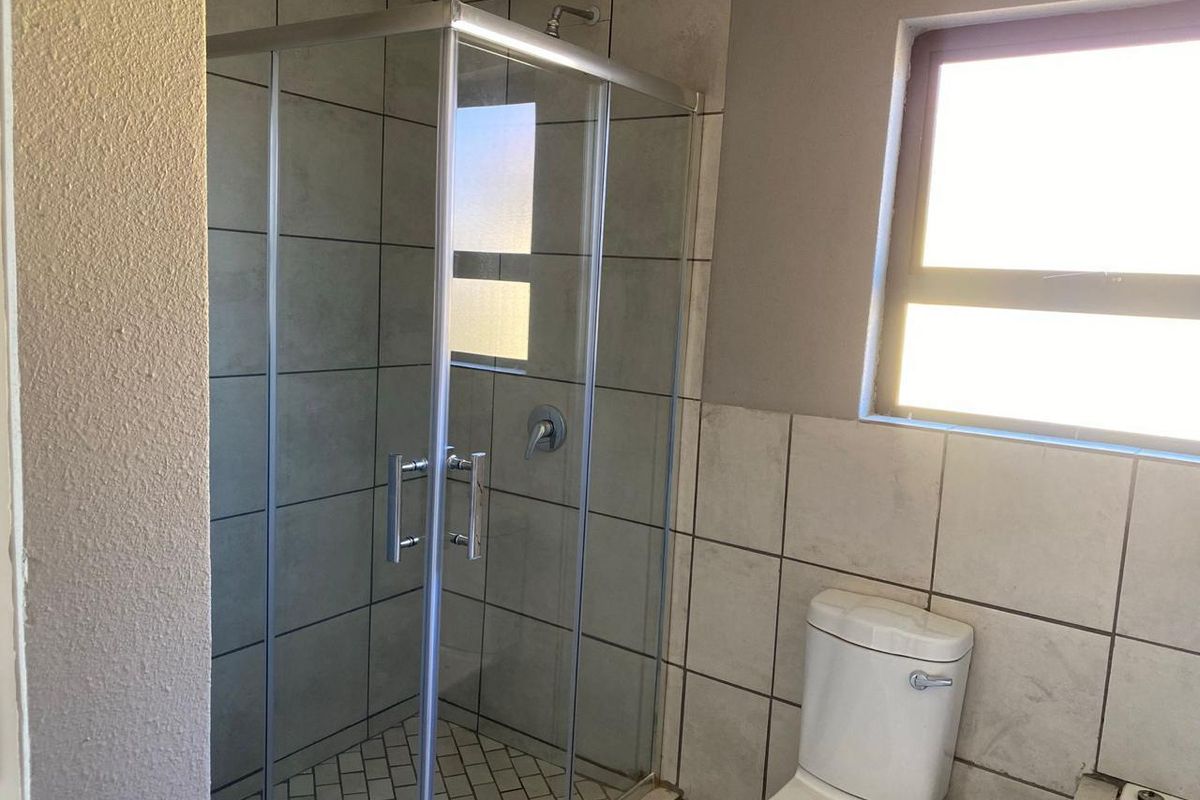 A functional bathroom featuring a glass-enclosed shower, tiled walls, and a standard toilet, offering a clean and neutral space.