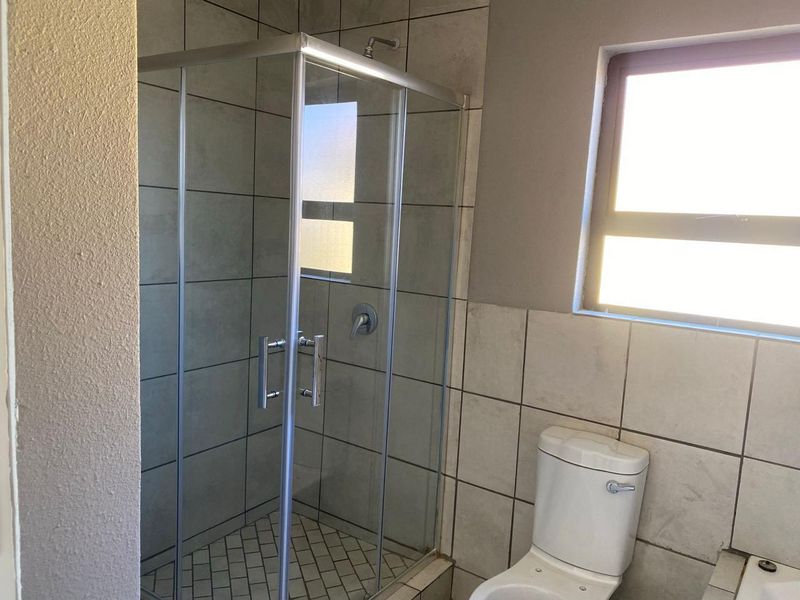 A functional bathroom featuring a glass-enclosed shower, tiled walls, and a standard toilet, offering a clean and neutral space.