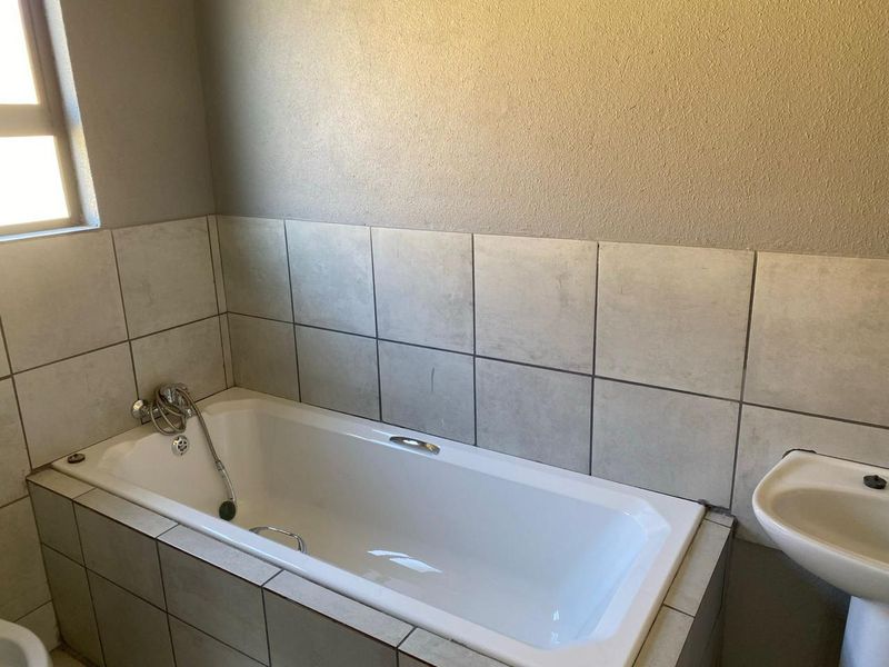 A functional bathroom featuring a built-in bathtub with a handheld shower attachment and a pedestal basin, finished with neutral wall tiling.