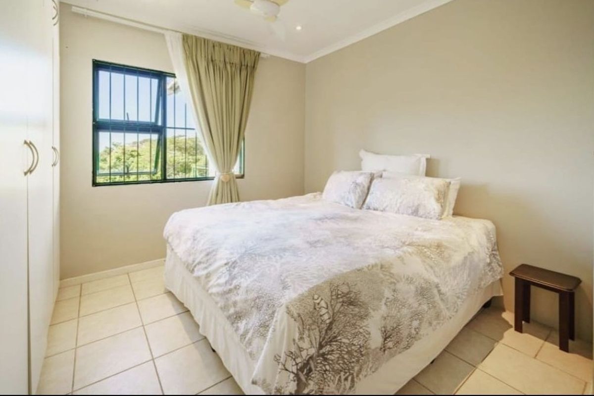 A functional bedroom featuring tiled flooring, built-in cupboards, a ceiling fan, and a window fitted with security bars.