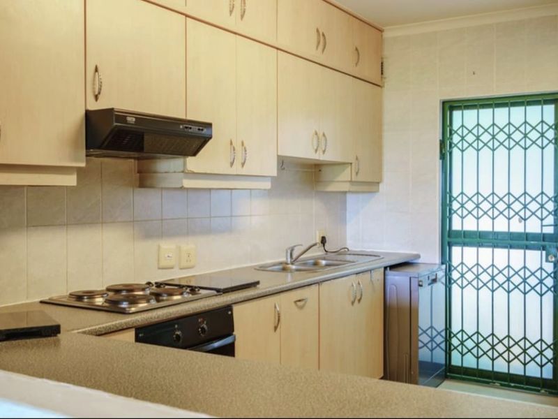 Functional kitchen featuring light wood-finish cabinetry, built-in oven, electric hob, extractor fan, and a tiled backsplash with direct access to an exterior security gate.