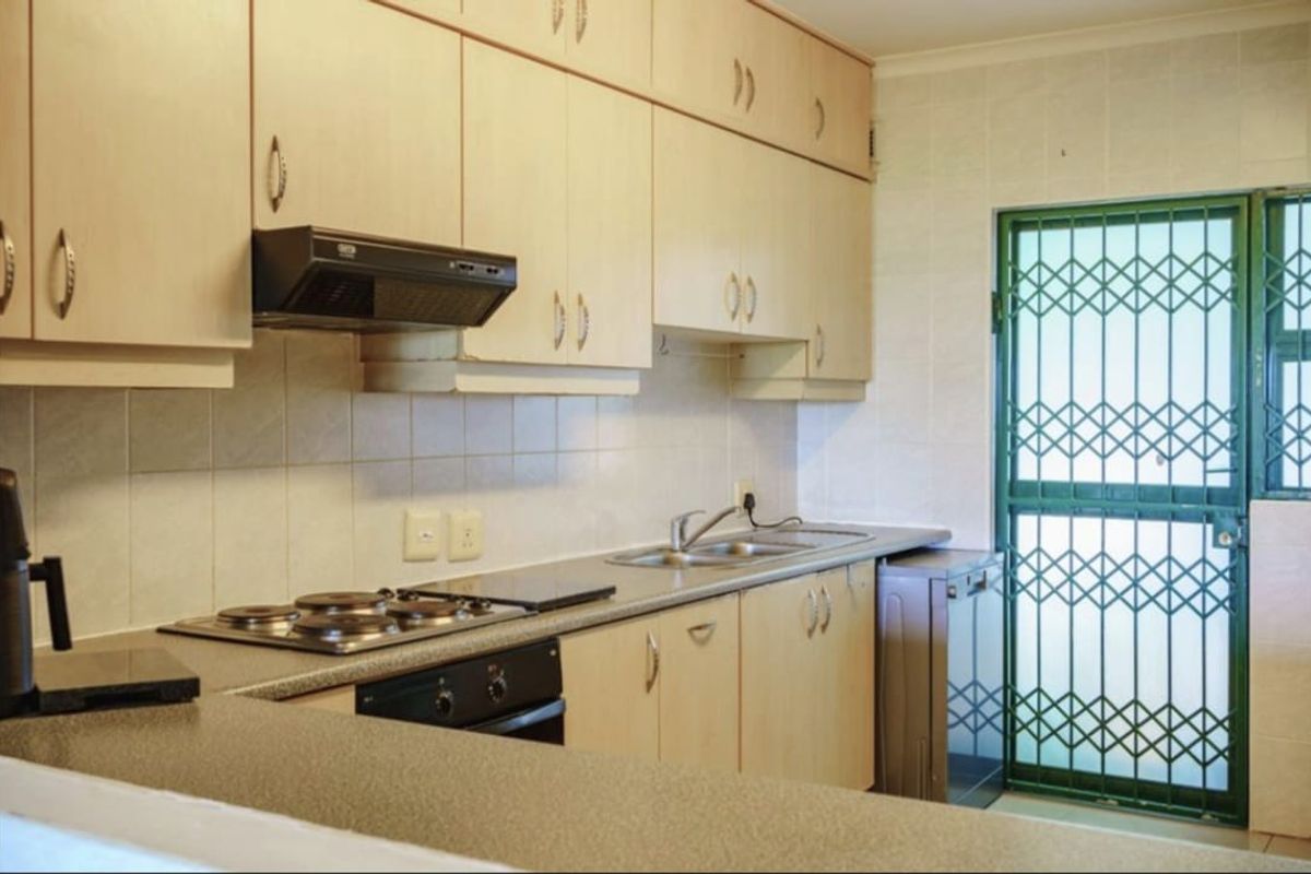 Functional kitchen featuring light wood-finish cabinetry, built-in oven, electric hob, extractor fan, and a tiled backsplash with direct access to an exterior security gate.