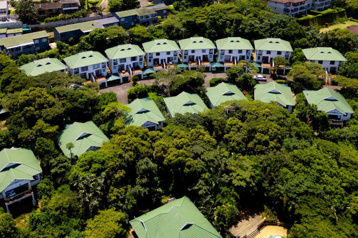 Aerial view of a residential apartment complex featuring multiple units with green pitched roofs set within a lush, tree-filled estate environment.