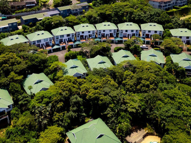 Aerial view of a residential apartment complex featuring multiple units with green pitched roofs set within a lush, tree-filled estate environment.