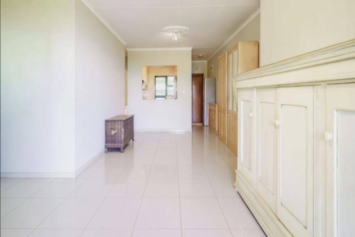 Spacious living area featuring neutral tiled flooring, built-in cabinetry, and a pass-through window connecting to the kitchen area.