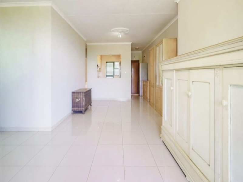 Spacious living area featuring neutral tiled flooring, built-in cabinetry, and a pass-through window connecting to the kitchen area.