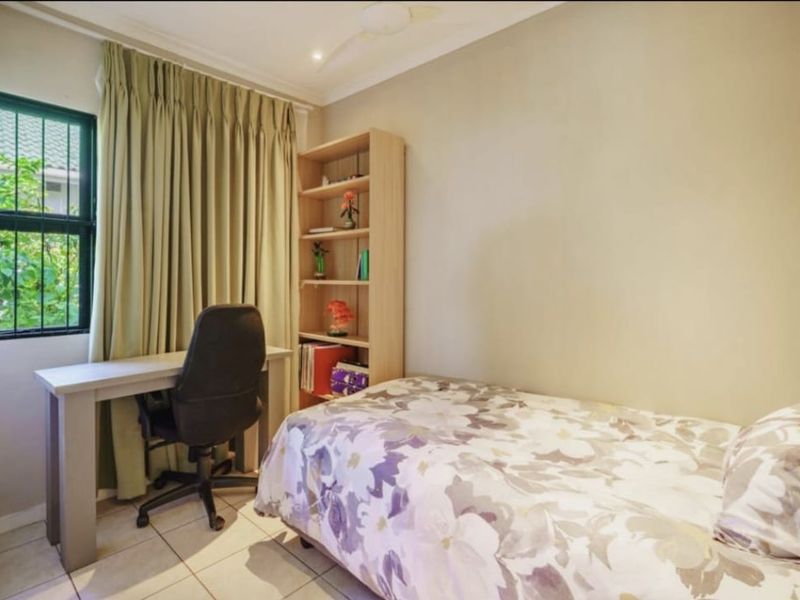 A functional bedroom featuring tiled flooring, a ceiling fan, and a window fitted with security bars.