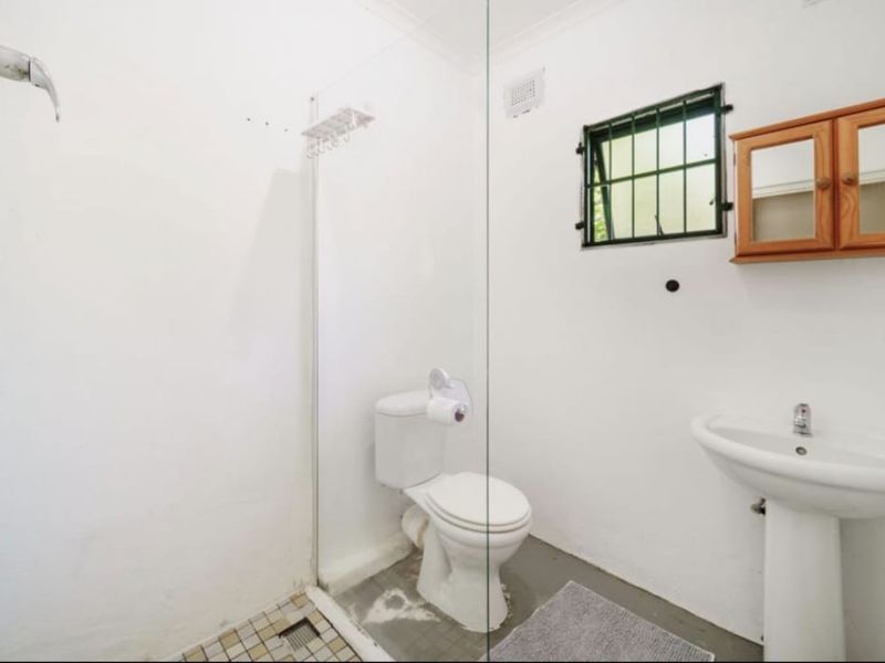 A functional bathroom featuring a pedestal basin, toilet, and a glass-enclosed shower area with a window for ventilation.
