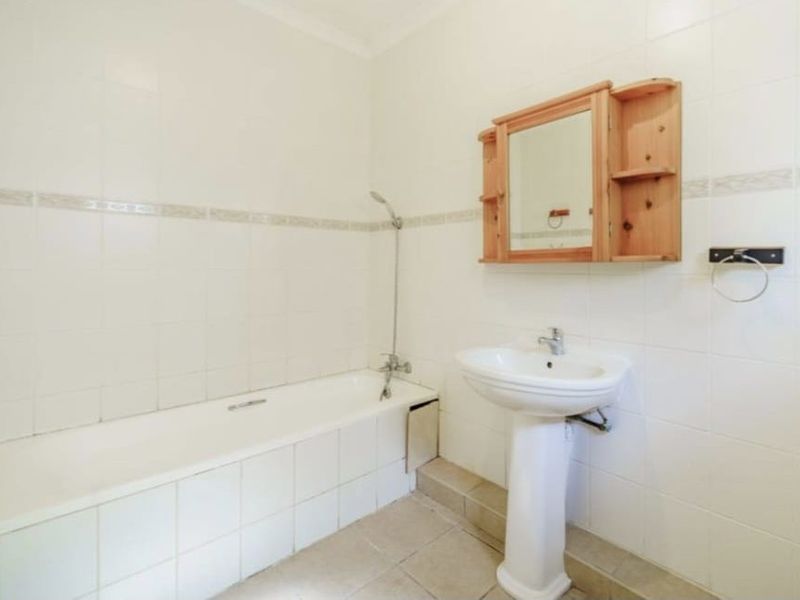 A functional bathroom featuring a pedestal basin, built-in bathtub with shower mixer, and neutral wall tiling.