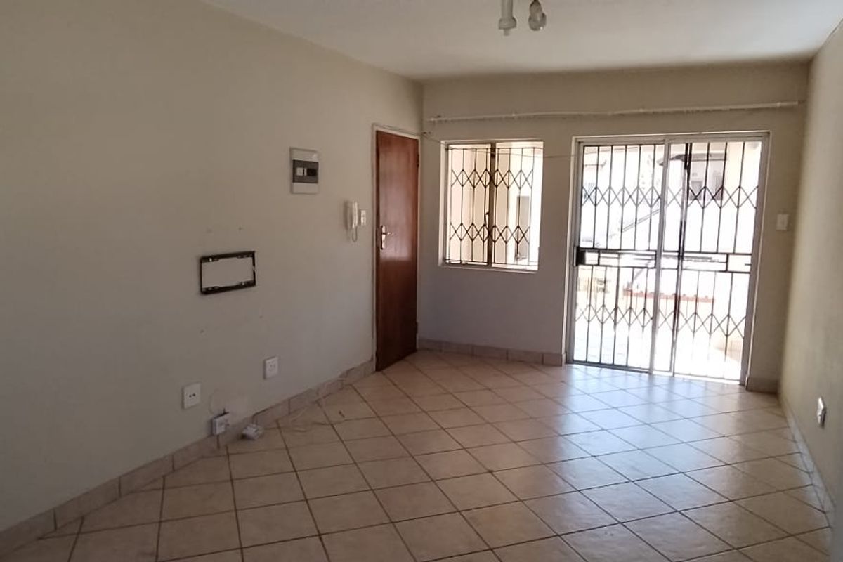 An empty living room featuring tiled flooring, a security gate, and a sliding door leading to an outdoor area.