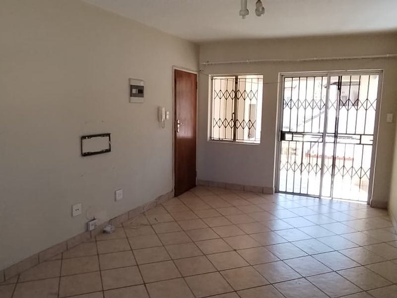 An empty living room featuring tiled flooring, a security gate, and a sliding door leading to an outdoor area.