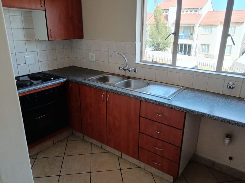 A functional kitchen featuring wood-finish cabinetry, laminate countertops, a double sink, and built-in electric cooking appliances with tiled flooring.
